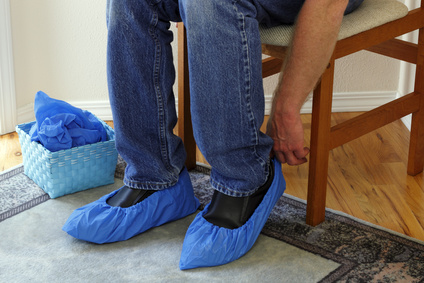 Male who just arrived in a foyer of a home for sale that he is going to tour sits in a chair putting booties on his shoes in order to protect the floors.